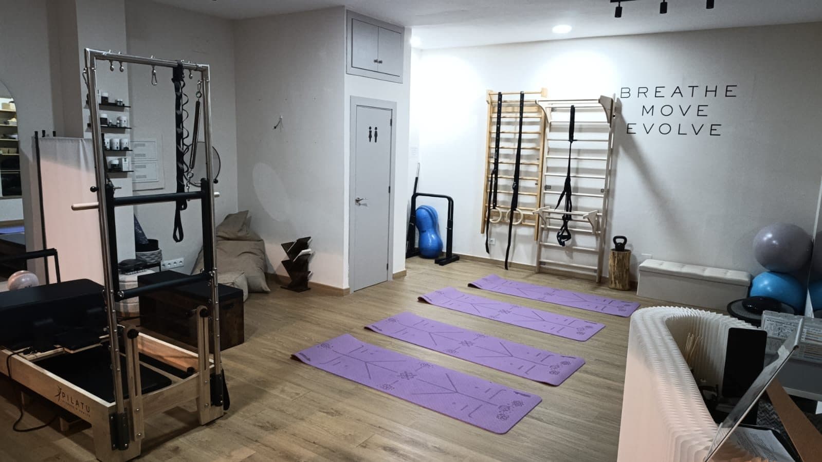 Sala de esterillas del estudio con espalderas, anillas y el lema Breathe Move Evolve en la pared